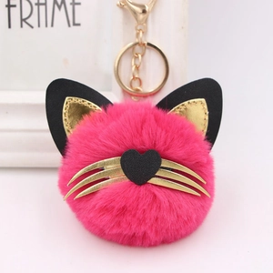 Close-up of pink fluffy cat head keychain with golden whiskers and heart nose detail