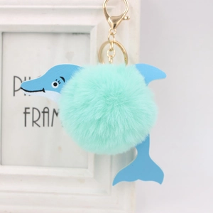 Close-up of a mint green fluffy pom pom dolphin keychain with gold metal clasp