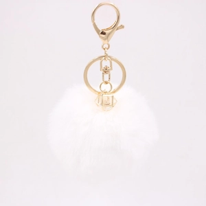 Detail of white faux rabbit fur pompom keychain with golden metal clasp and gemstone bead