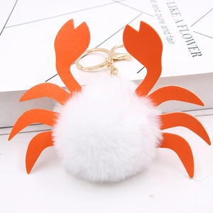 Détail du porte-clés crabe en peluche blanche avec pinces en similicuir orange et métal doré