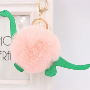 Close-up of pink pompom dinosaur keychain with green textured leather and gold clasp