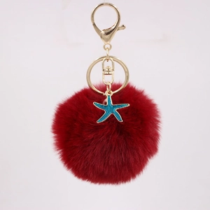 Close-up of deep red faux fur pompom keychain with golden clasp and blue enamel star charm