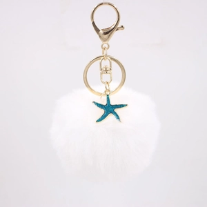 Close-up of white fluffy pompom keychain with golden metal clasp and blue starfish charm