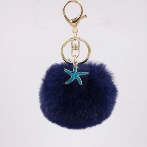 Close-up of fluffy dark blue pompom keychain with golden clasp and starfish charm