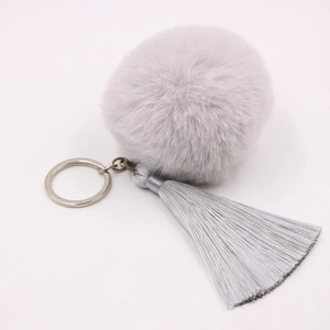 Detailed macro view of a fluffy grey faux fur pom pom keychain with silky fringe tassels