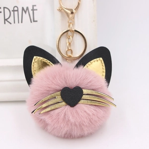 Close-up of pink plush cat head keychain with gold whiskers and a black heart nose charm