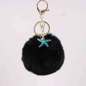 Detail of black faux fur pompom keychain with teal starfish charm and gold lobster clasp