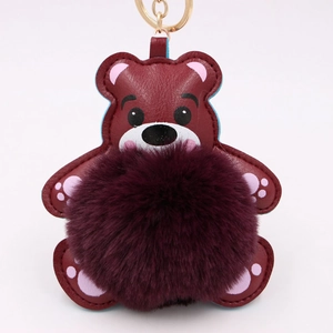 Gros plan du porte-clés ours en cuir bordeaux avec pompon violet et anneau doré