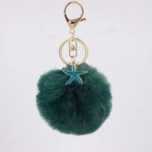 Detailed view of dark green fluffy pompom keychain with teal starfish and gold metal clasp