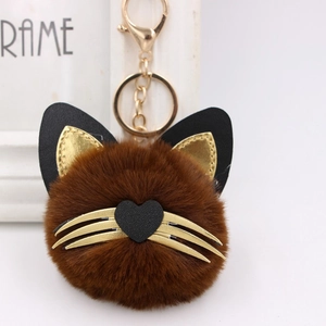 Detail of plush cat keychain with brown fur ball, gold whiskers, and heart nose
