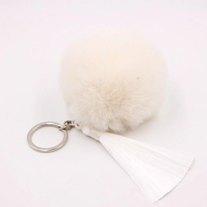 Detailed view of fluffy off-white faux fox fur pom pom with long silky white tassels