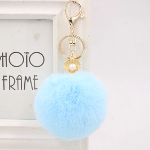 Detail view of light blue faux fur pompom keychain with golden seashell and pearl charm