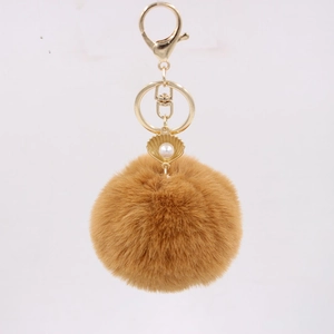 Detailed macro of brown faux fur pom pom keychain with gold shell and white pearl decor