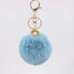 Detailed close-up of light blue fluffy pompom keychain with golden shell and pearl charm