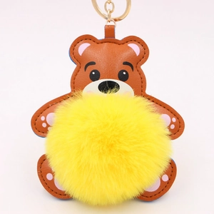 Détail d'un porte-clés ours en cuir marron avec pompon jaune et anneau en métal doré