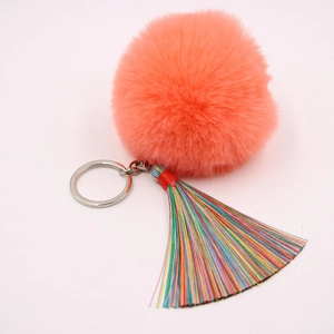 Detail eines pfirsichfarbenen Pelz-Pompons mit buntem Quasten-Anhänger und Silberring