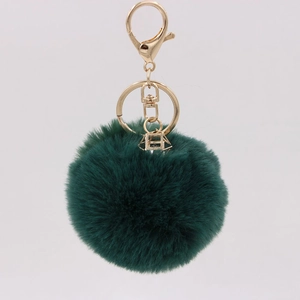 Close-up of fluffy dark green faux fur keychain with gold lobster clasp and geometric charm