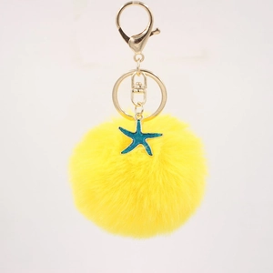 Macro detail of a yellow pompom keychain with a blue starfish charm and gold lobster clasp