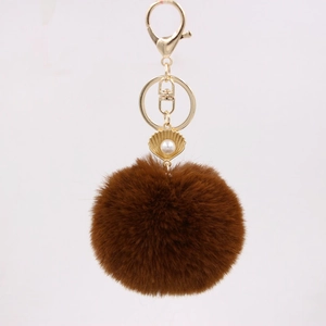 Detail of a brown faux fur keychain featuring a gold shell pendant and white faux pearl