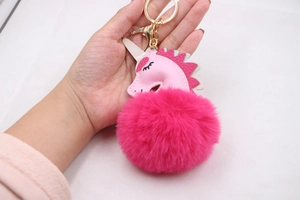 Detailed close-up of pink leather unicorn and fluffy rose red pompom keychain accessory
