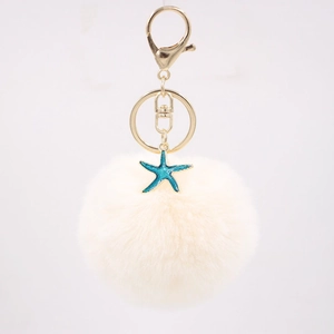 Detailed close-up of cream faux fur pompom keychain with blue starfish and gold clasp