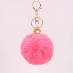 Close-up of pink fluffy pompom keychain with golden shell and pearl detail