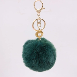 Detail of dark green faux fur pompom keychain with a golden shell and pearl charm