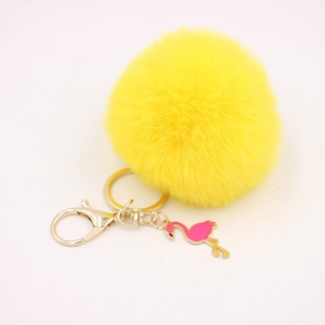 Detail of yellow plush pompom keychain with golden clasp and pink flamingo charm