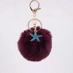 Detail of dark purple faux fur pompom keychain with blue starfish pendant and gold clasp
