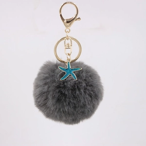 Detail of dark grey faux fur pompom keychain with golden metal ring and teal starfish charm