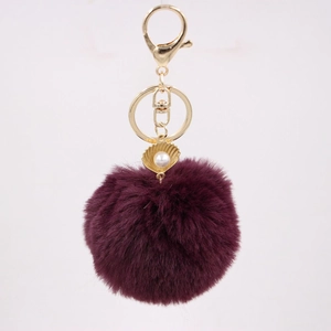 Detailed view of dark purple faux fur pompom keychain with golden shell pearl charm