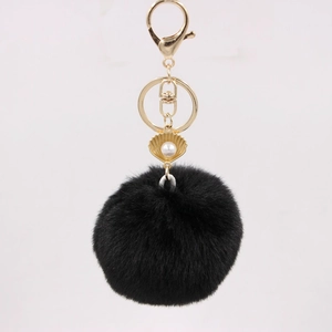 Detail of black faux fur pompom keychain with gold seashell pendant and white pearl