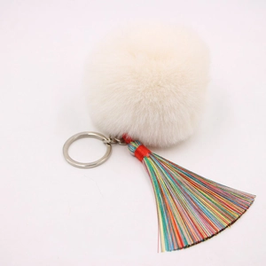 Detailansicht eines weißen Kunstfell-Pompons mit buntem Quastenanhänger und Silber-Schlüsselring