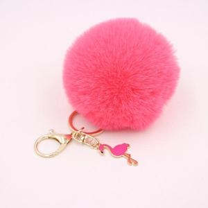 Detail of pink fluffy pompom keychain with golden clasp and cute flamingo pendant charm