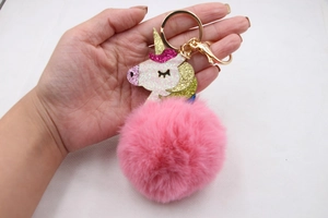 Close-up of pink faux fur pompom keychain with sequined unicorn head and golden clasp