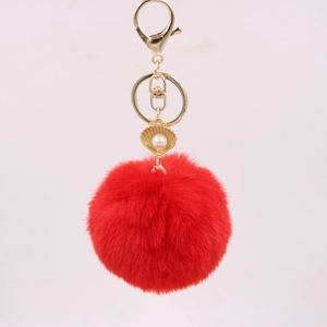 Detail of red faux fur pompom keychain with golden shell charm and white pearl