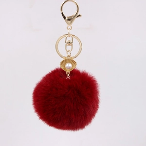 Detailed macro view of a red fluffy pompom keychain with golden shell and pearl charm
