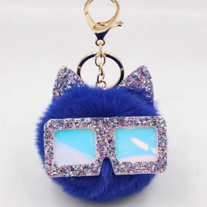 Détail d'un porte-clés pompon bleu foncé avec oreilles de chat à paillettes et lunettes