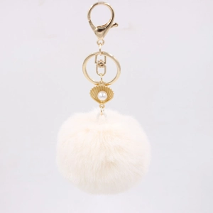 Detail of soft faux fur pompom keychain with golden shell and pearl charm element