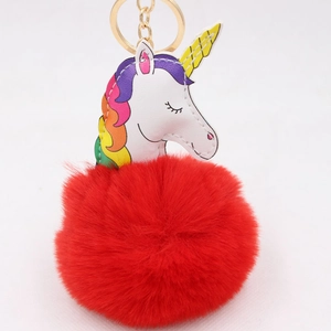 Détail d'un pompon rouge en peluche avec un charm de licorne en similicuir blanc et doré