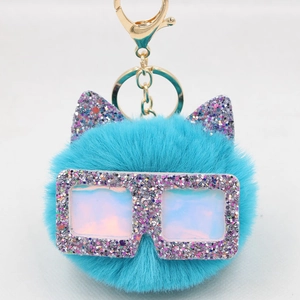 Détail d'un porte-clés en peluche bleue avec oreilles de chat et lunettes pailletées