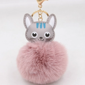 Détail d'un porte-clés à pompon rose avec un charm de tête de chat en similicuir gris