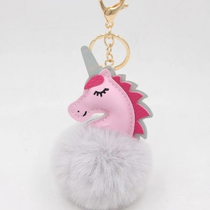 Detailed view of a pink unicorn plush keychain with a soft grey fur pom pom and gold clasp