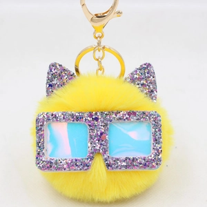 Détail de porte-clés pompon jaune avec oreilles pailletées et lunettes holographiques