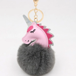 Close-up of pink leather unicorn head and dark grey fluffy pompom with golden metal clip
