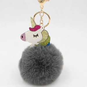 Close-up of colorful glitter unicorn head with gray faux fur pompom on gold keychain