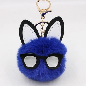 Detail of dark blue plush rabbit pom-pom keychain with black-rimmed glasses and golden hook