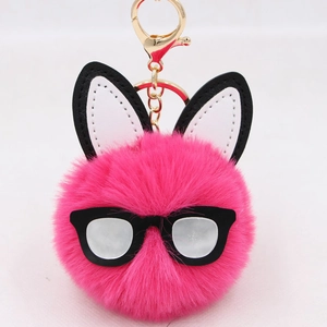 Close-up of pink fluffy pom-pom rabbit keychain with black glasses and gold hardware