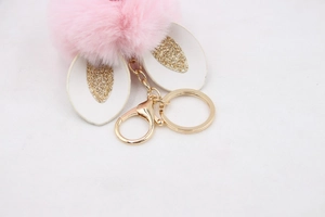 Close-up of pink fluffy pompom keychain with sequined white bunny ears and golden metal clasp
