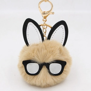 Detail of plush bunny keychain with brown fur ball, black spectacles and golden clasp